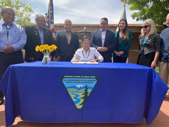 Secretary Haaland signing document at a table with others standing behind her. 