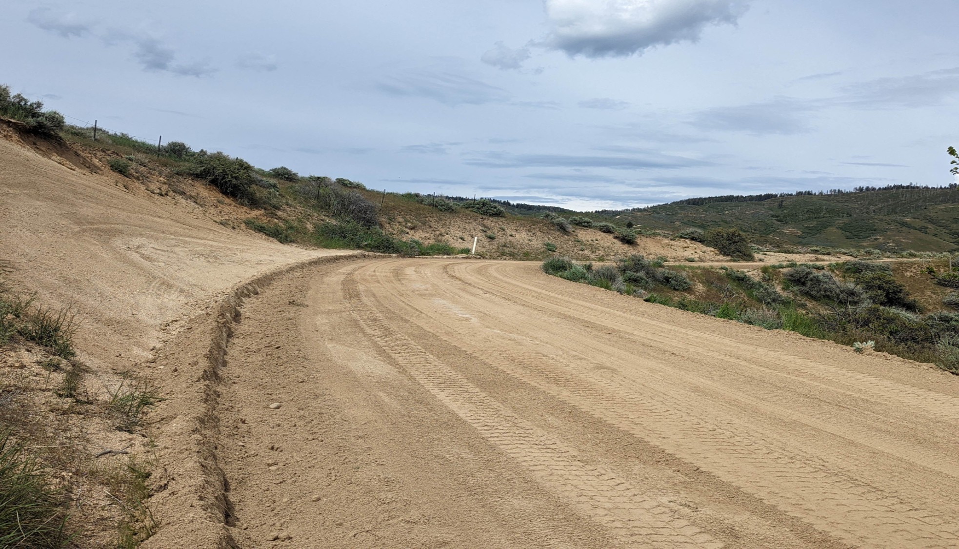Dirt road cleared of surface hazards winds through dry, hilly landscape.