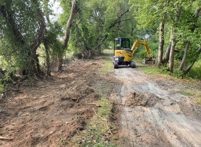 Yellow excavator clears path on lush, forested trail