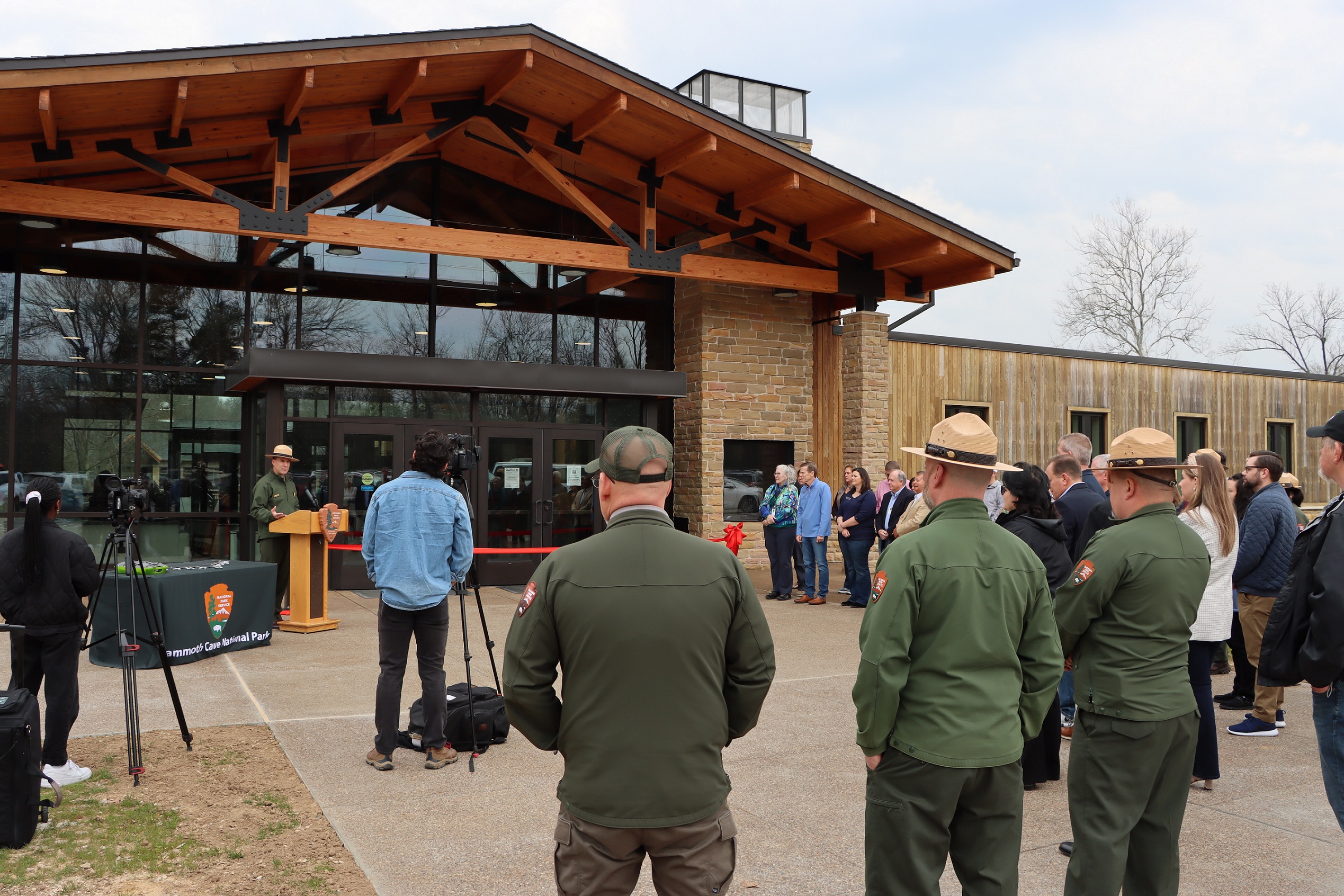 The Park Superintendent addresses a crowd of people from a podium in front of the renovated Mammoth Cave Lodge