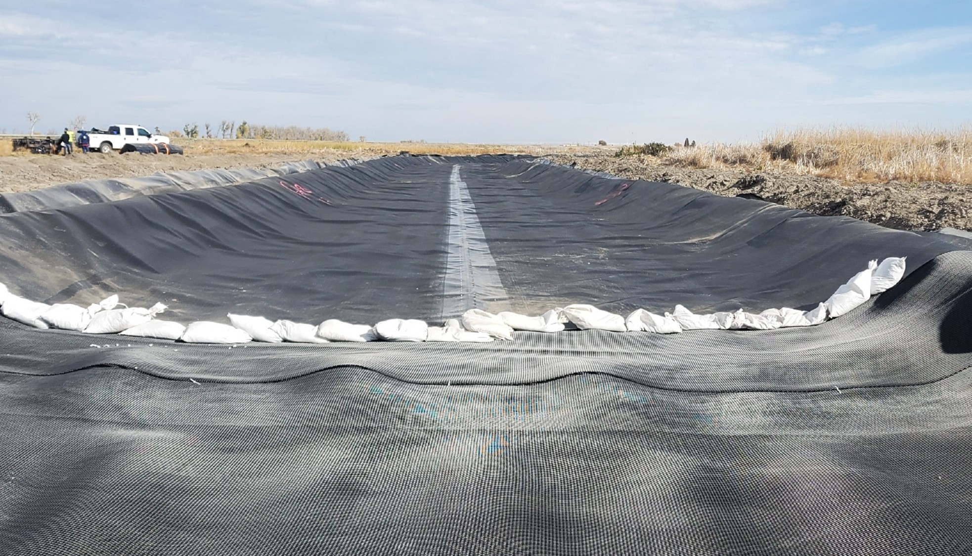 Black impervious lining covers shallow path through a dry landscape.