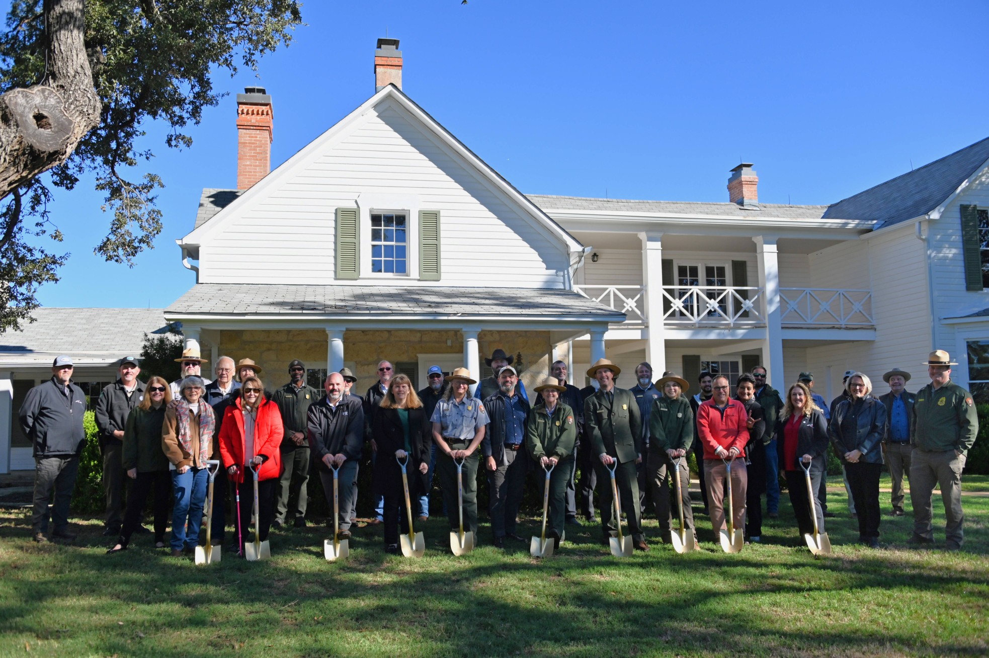 Group of people holding shovels pose together in front of newly renovated house.