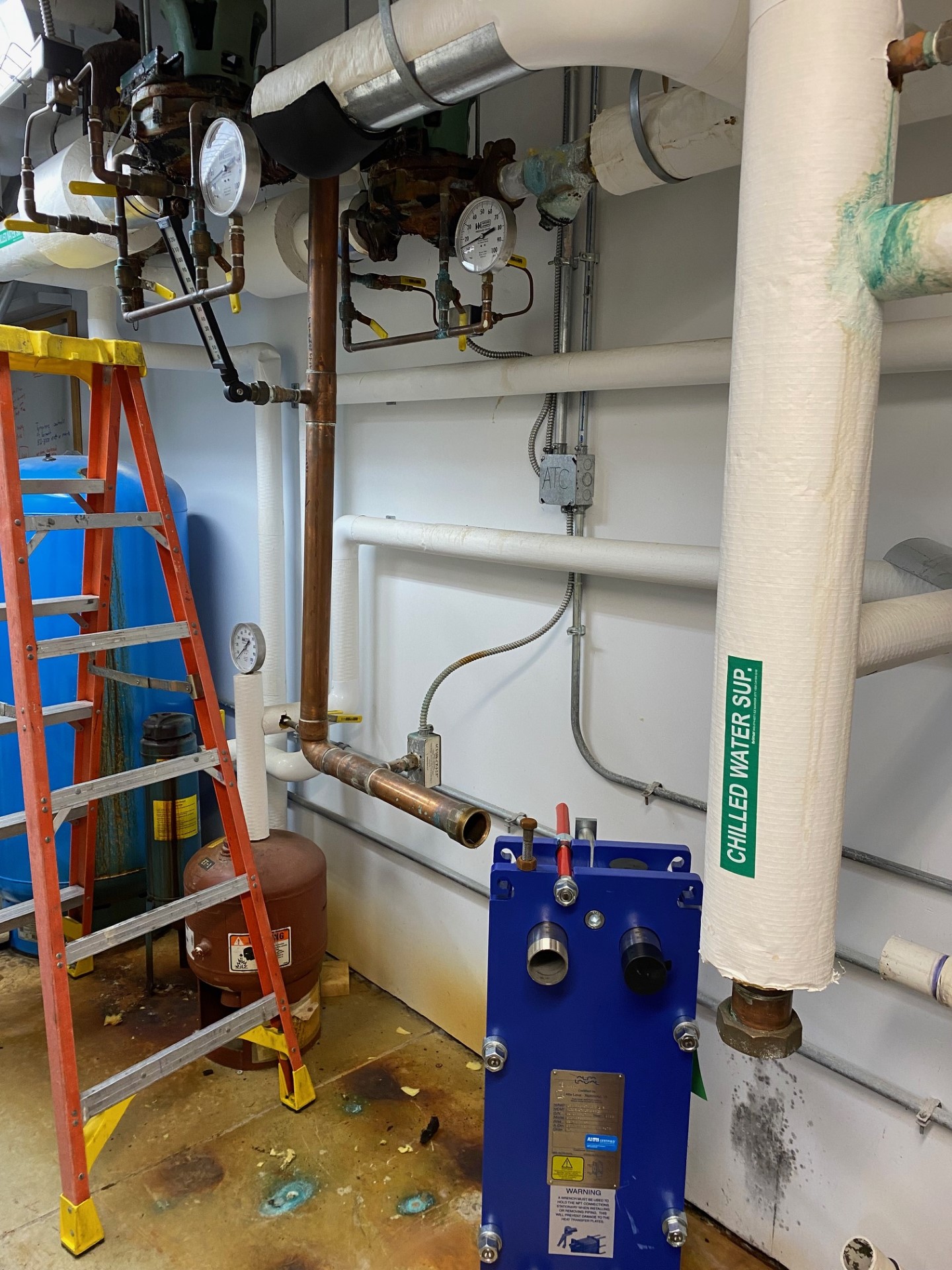 Orange ladder sits next to a heat exchanger system in a utility room.