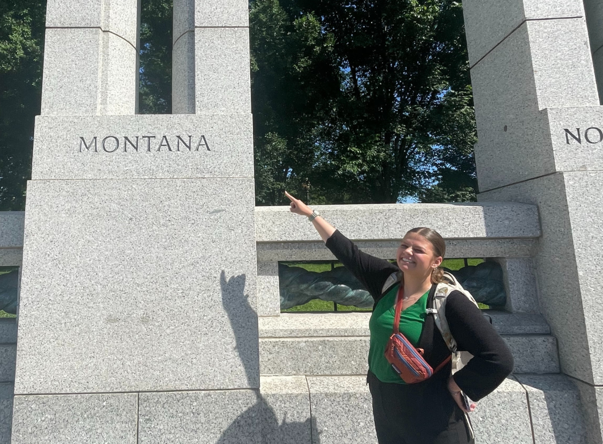 Zoe Belinda, Office of Wildland Fire intern, standing next to the Montana block of the World War II Memorial in Washington D.C. She points to the word "Montana."