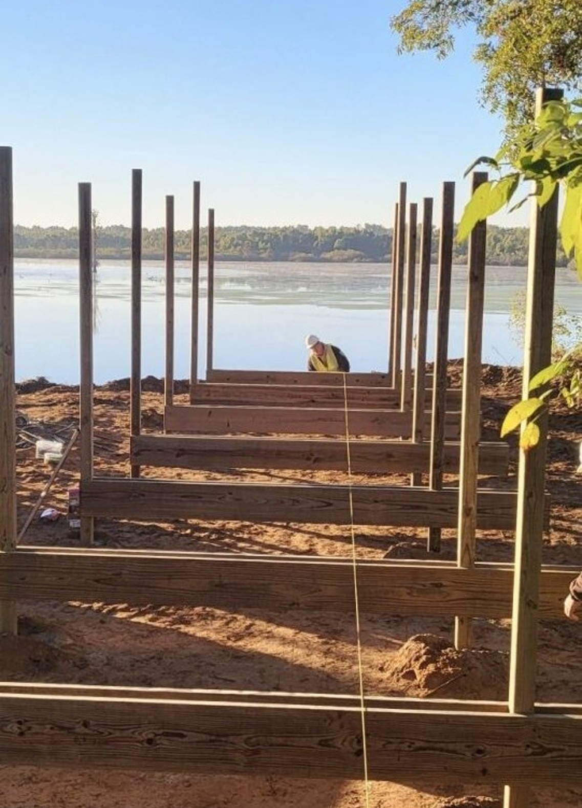 Construction worker stands at the end of new boardwalk base with lake in the background.