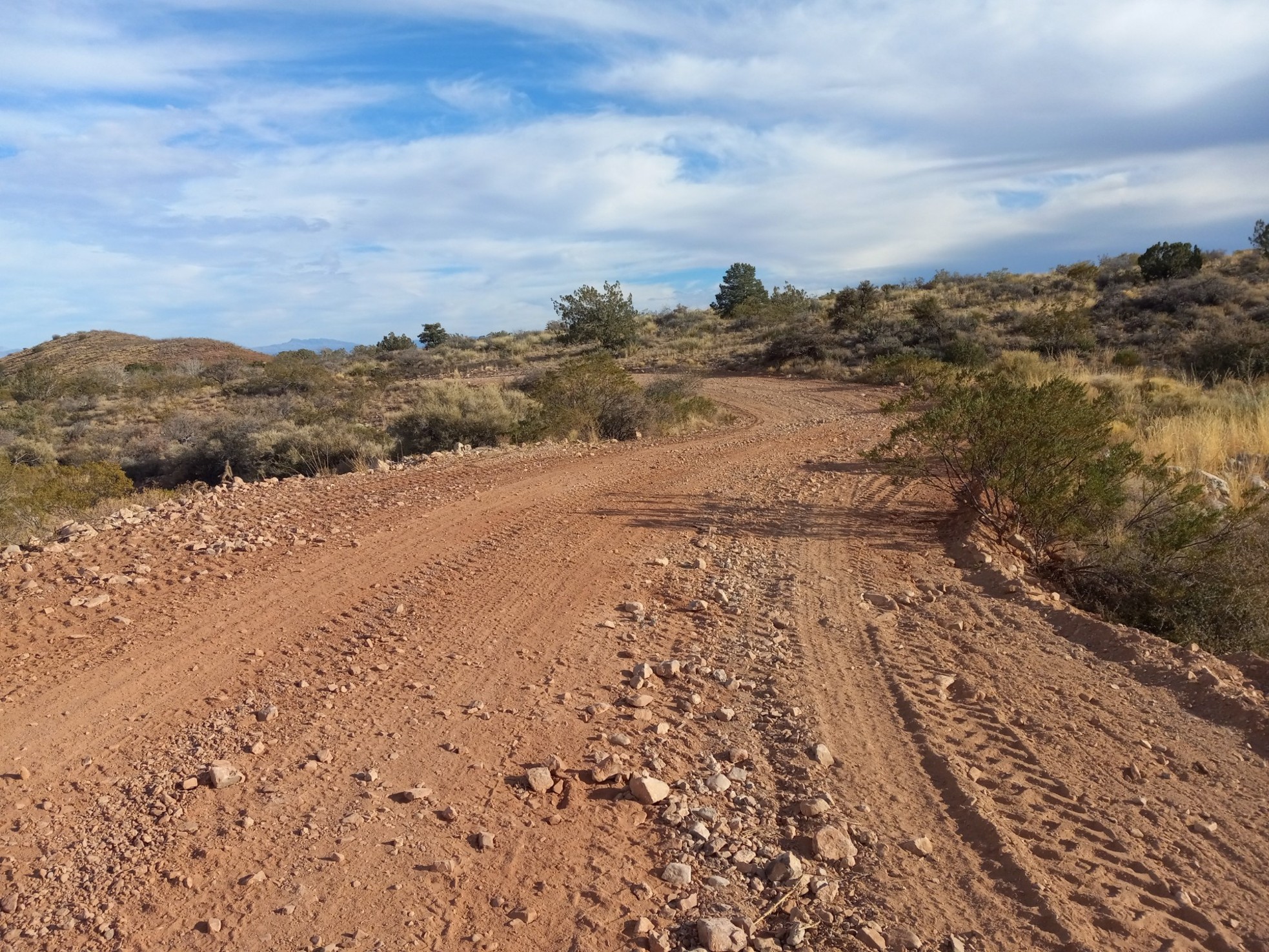 A dirt road free of surface hazards winds through dry, hilly landscape.