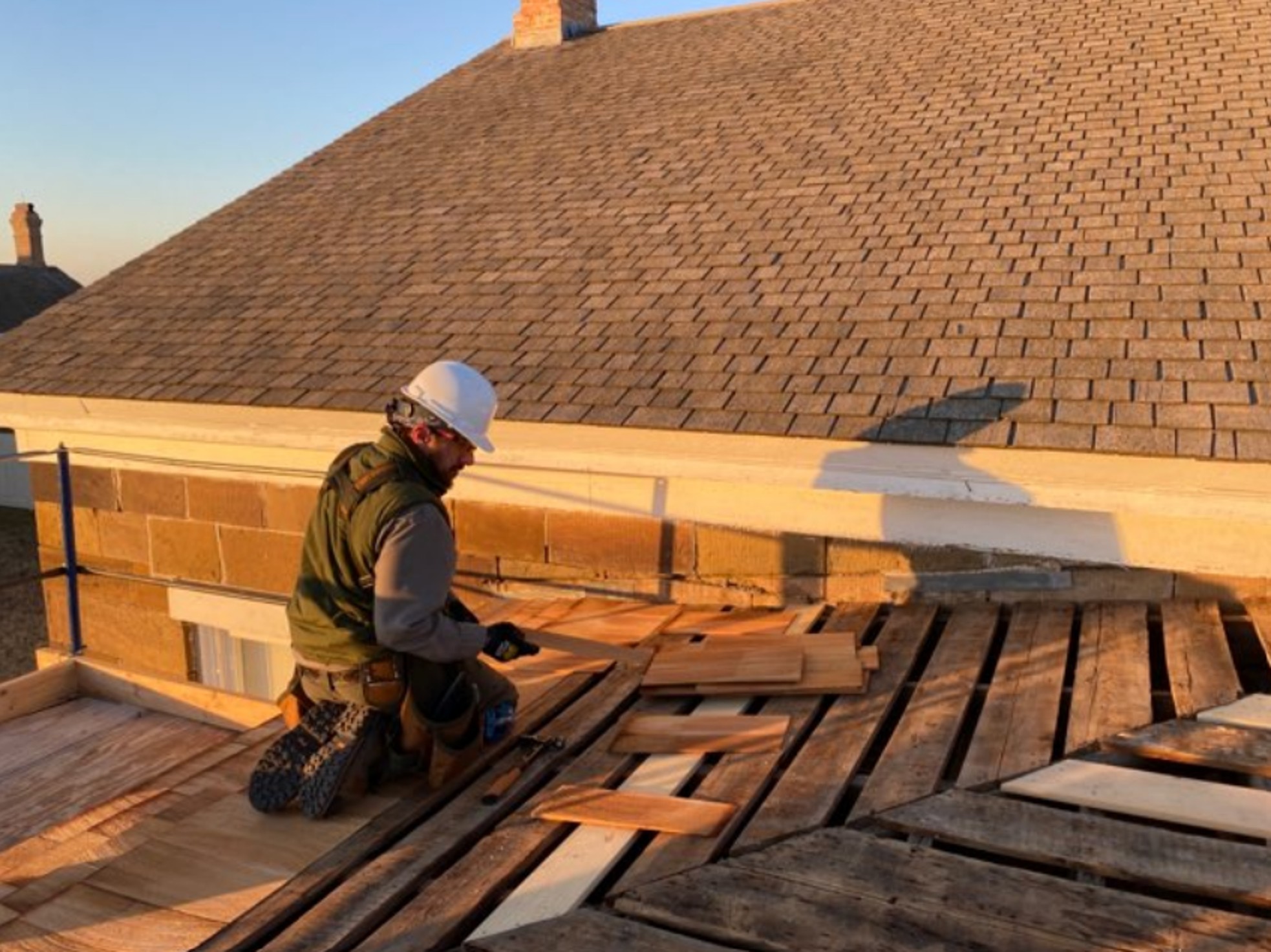 Construction worker sits on scaffolding against the roof of quarters building.