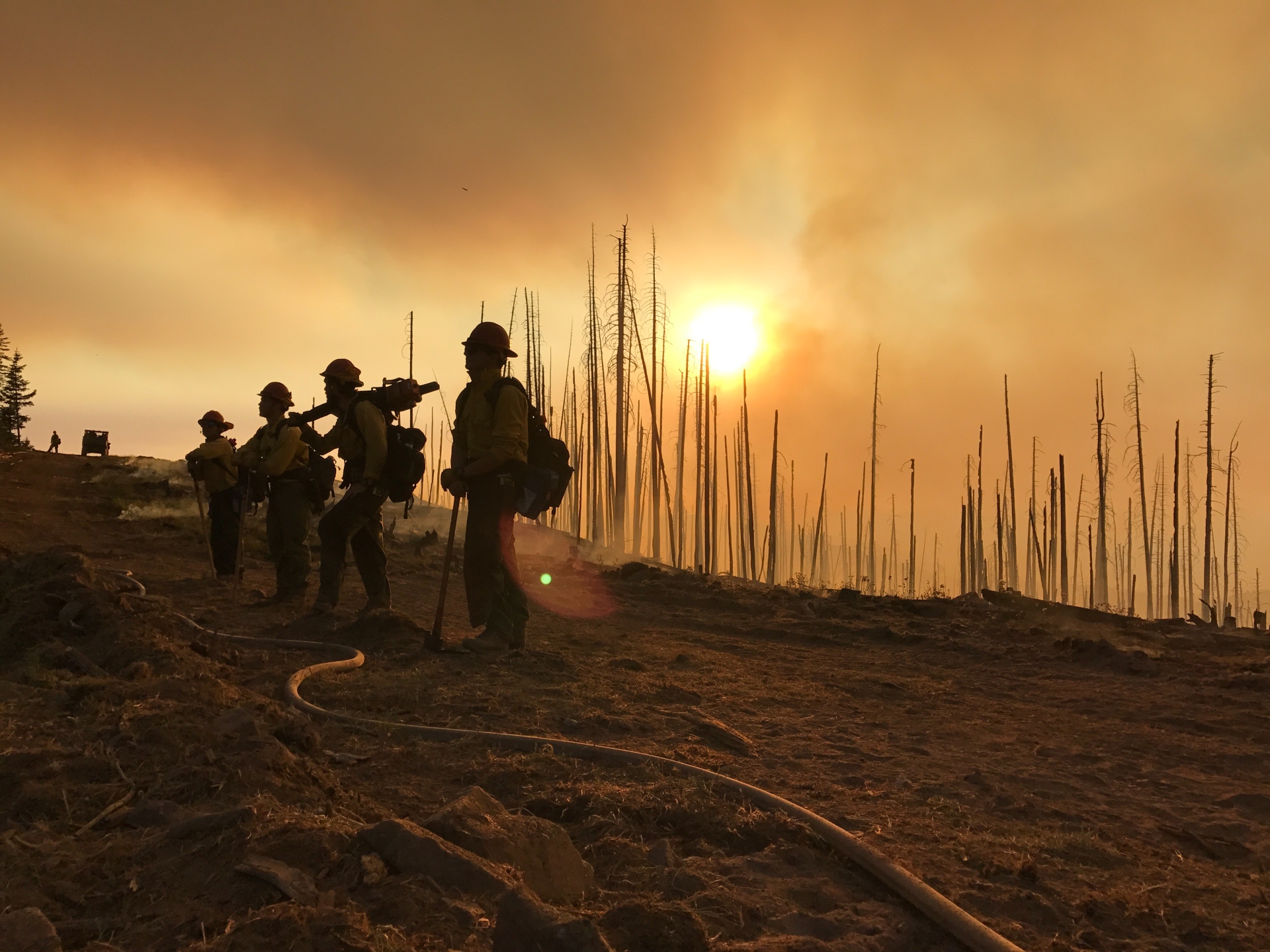 Firefighters are silhouetted by a setting sun, with smoke in the background. DOI image 