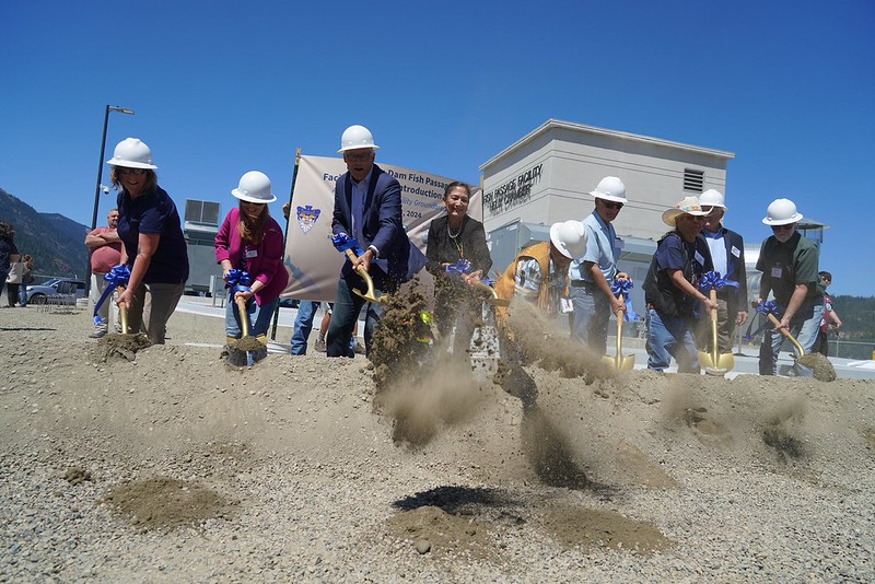 Group of people in white hard hats digging into ground with shovels.