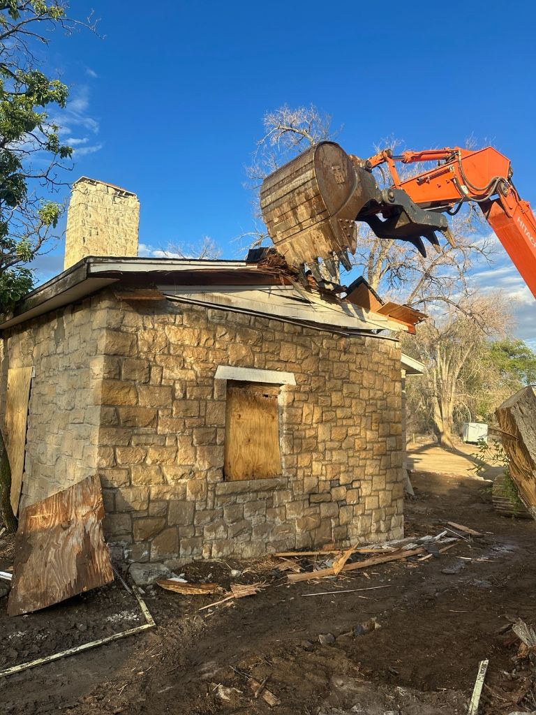 Orange construction vehicle demolishes gray brick facility building.