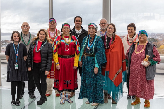 A group of Native Americans in traditional dress stands with DOI-ITAP staff