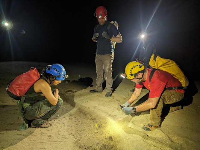 Three people examine the floor of a cave in Belize