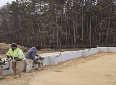 Two men stand next to short concrete wall surrounding a dirt plot.