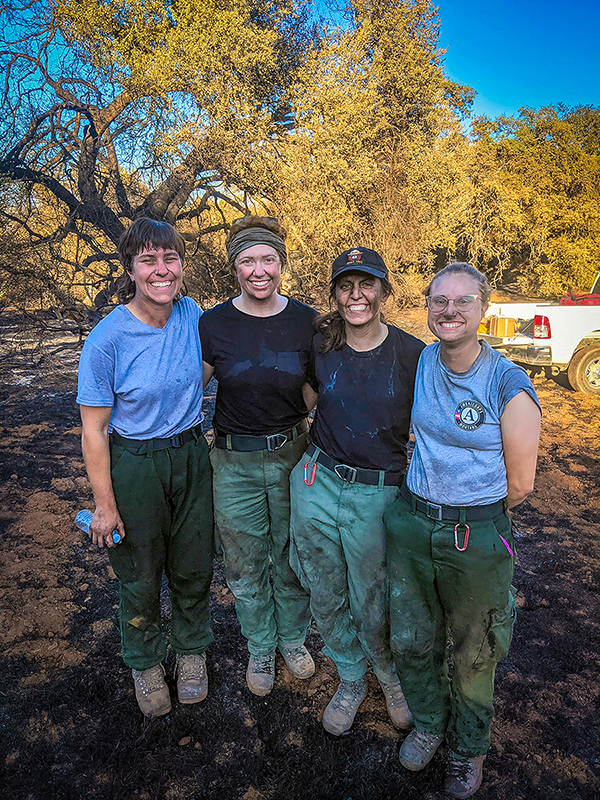Four smudged members of the all-women conservation corps fire crew at Grand Teton National Park pose for a photo in a fire-blackened clearing. (Photo by NPS.)