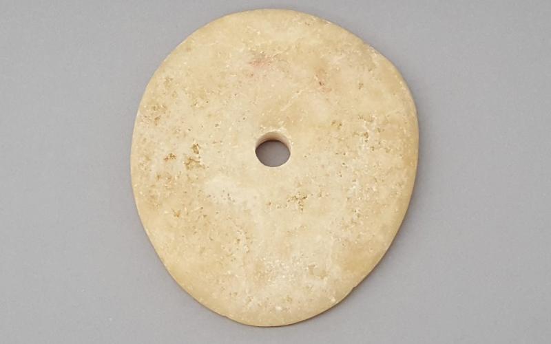 Flat, thin, and circular stone with a small hole in the middle.