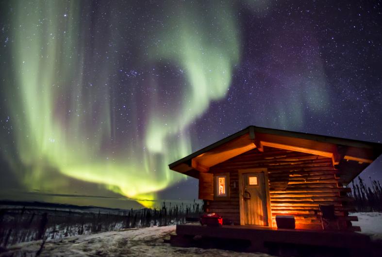 Wooden cabin under a starry sky with northern lights.