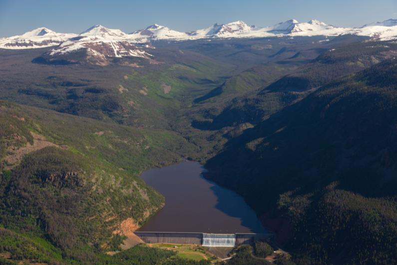 Aerial view of snow covered Uintah Mountains in the background with Upper Stillwater reservoir and dam in the foreground.