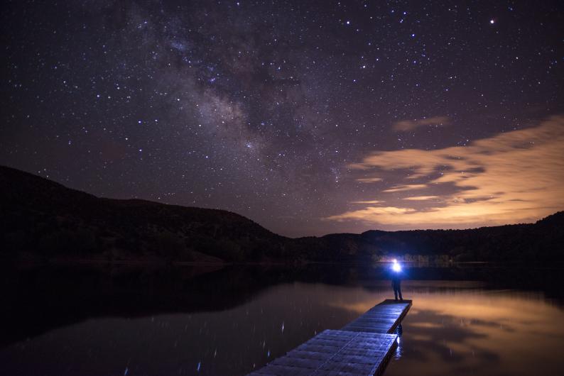 Person stands at the end of a dock under a starry sky.