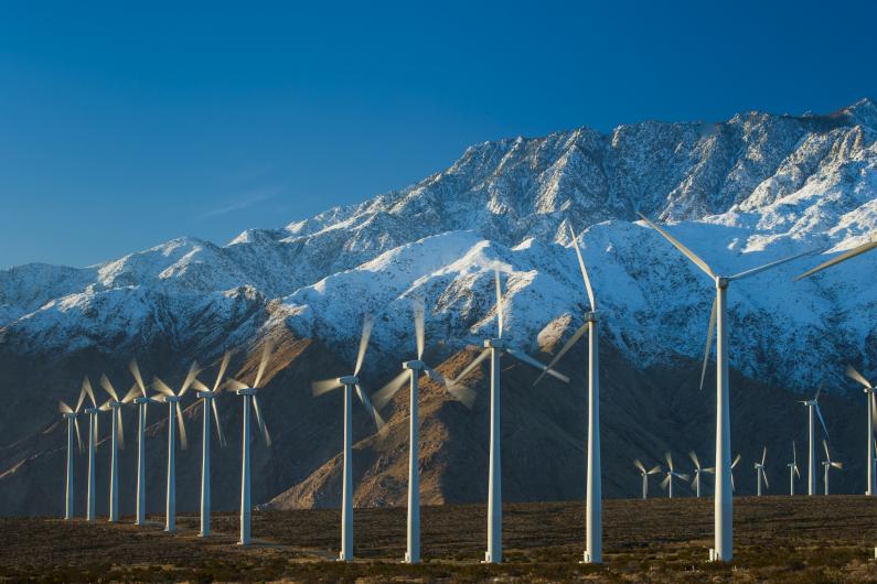 Wind turbines in front of a snowy mountain range.