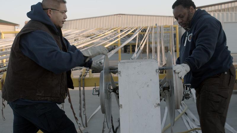 Two employees clean and repair fire equipment at a fire facility. 