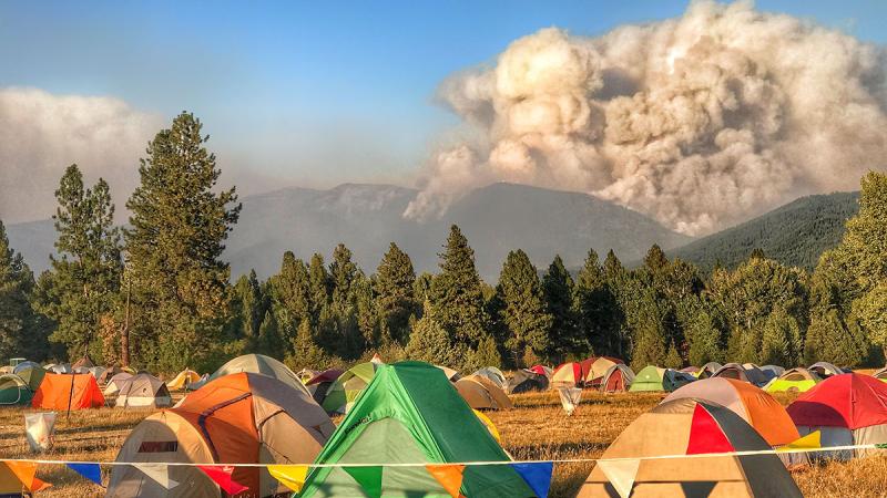 Tents arrayed in a fire camp as smoke from a wildfire rises in the distance. Photo by Clayton Schmidt, BLM.