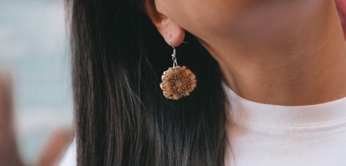 Photograph of a carved antler earring hanging from a woman's ear.