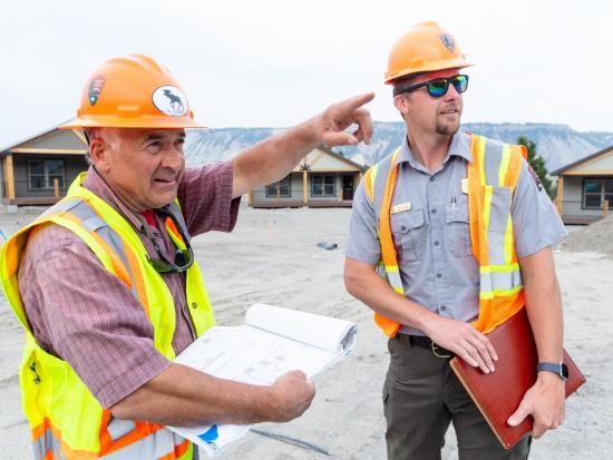 Two engineers with hard hats observe a building site.