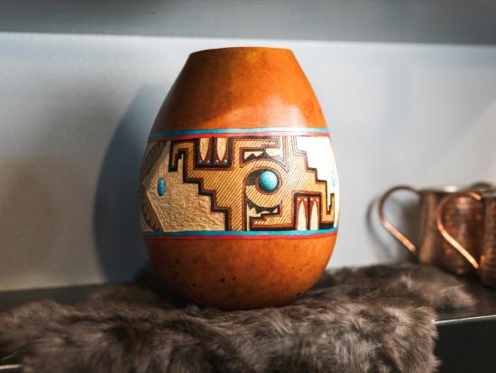 Photograph of a gourd with a painted brown, blue, and black geometric design.