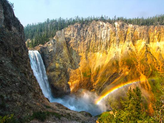 Waterfall over rocky cliff with rainbow at the bottom.