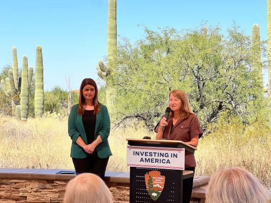 Acting Deputy Secretary Daniel-Davis standing behind podium in desert landscape.