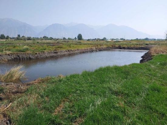 River in flat grassy area with mountains off in the distance.