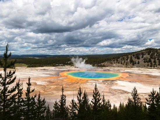 Bright colored hot spring with steam and a cloudy sky. 