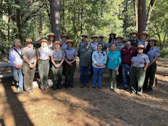 Secretary Haaland and large group of National Park Service employees in a wooded area near a picnic table. 