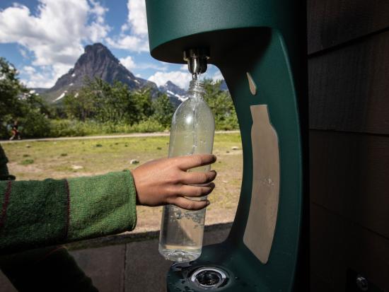 Ranger fills up a water bottle at water bottle filling station in front of mountain landscape. 