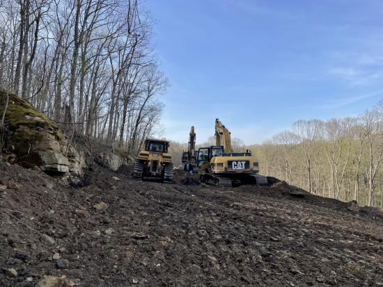 Three yellow excavators in a rocky dirt area. 