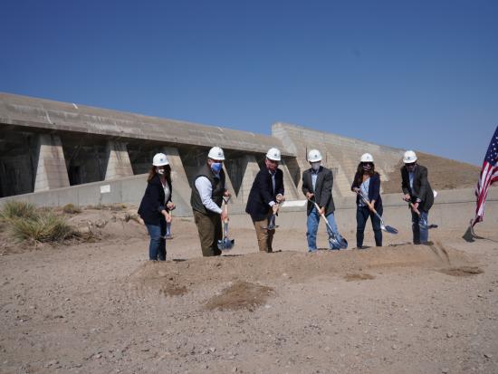 A small group of people use ceremonial shovels for a groundbreaking ceremony outside.