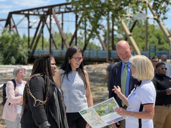 Assistant Secretary Shannon Estenoz and group of people talking in front of a bridge