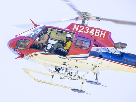 Four crew members look out from a helicopter in the sky.