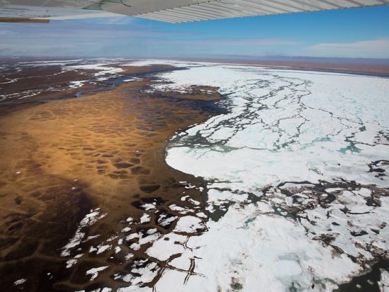 Aerial view of a flat plain covered in brown grass and white snow.