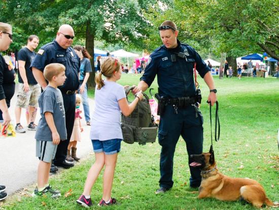 K9 officer hands a tactical bullet proof vest to a little girl during a demonstration while his dog lies beside him.