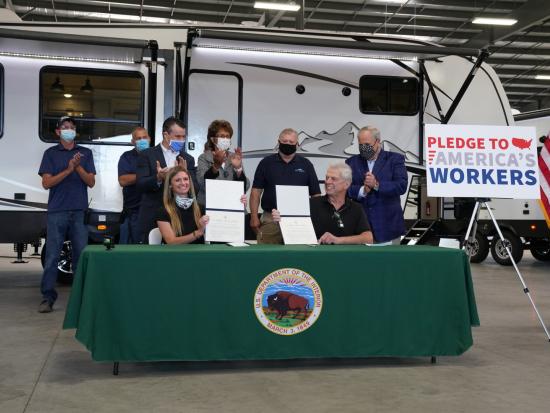 A small group of people stand around a table in an RV factory.