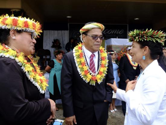 Secretary Haaland wearing a floral headpiece conversing with two people wearing floral headpieces and leis. 