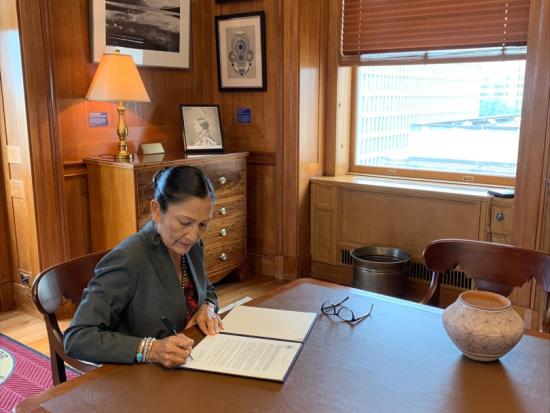 Secretary Haaland at a wooden table signing the Confederated Salish and Kootenai-Montana Compact.