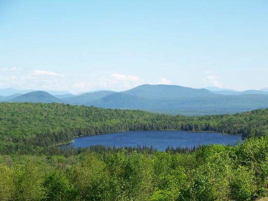 Deep blue pound surrounded on each side by a thick forest with a mountain range in the background.