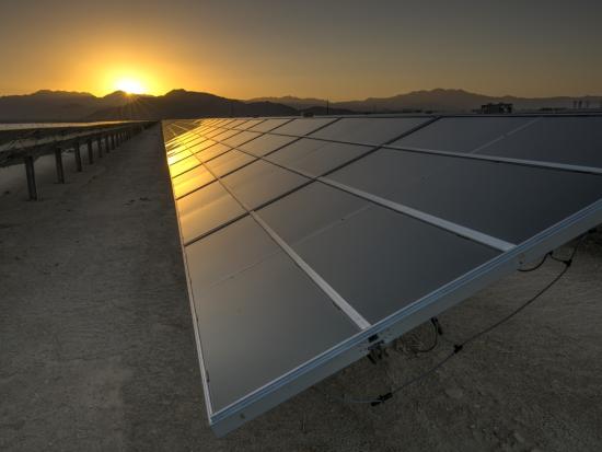 Sun setting and reflecting off of solar panels in a desert landscape. 