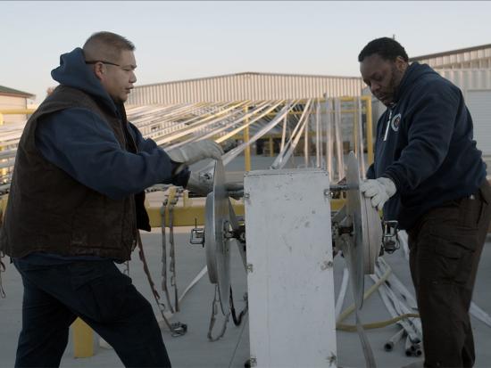 Two employees stand at a hose cleaning station as they repair hose. 