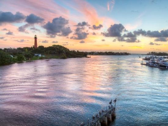 Pastel sunset over a lighthouse, with water and groups of boats