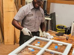 A member of the Maintenance Action Team in NPS uniform glazing a window on a wooden table