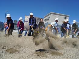 Group of people in white hard hats digging into ground with shovels.