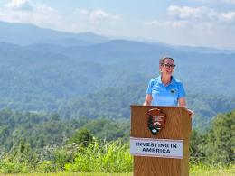 Assistant Secretary Estenoz standing behind NPS podium, rolling hills in the backdrop. 